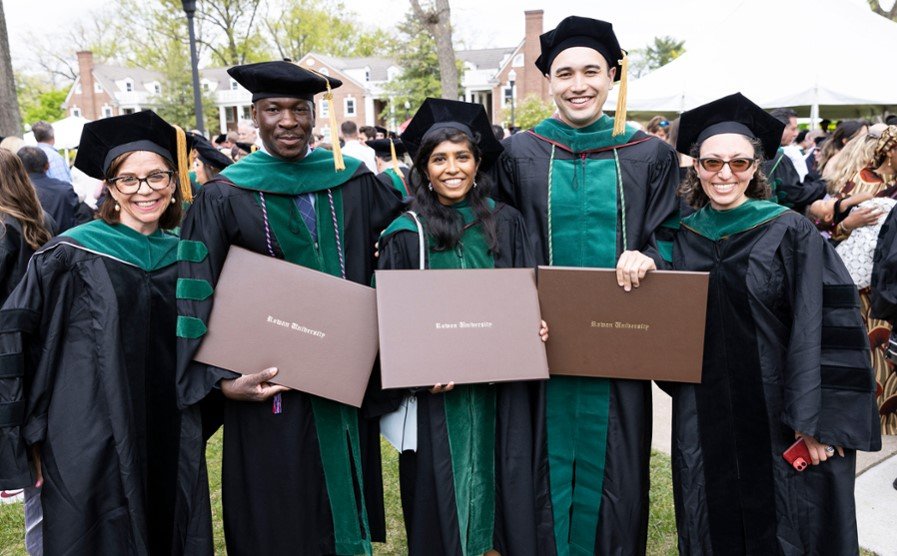 A photo of recent CMSRU graduates posing for a photo while holding their diploma covers at their Commencement ceremony.