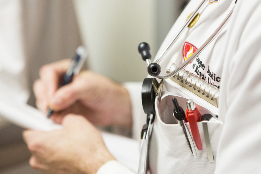 A close-up photo of a medical student taking notes on a notepad while wearing their CMSRU White Coat.