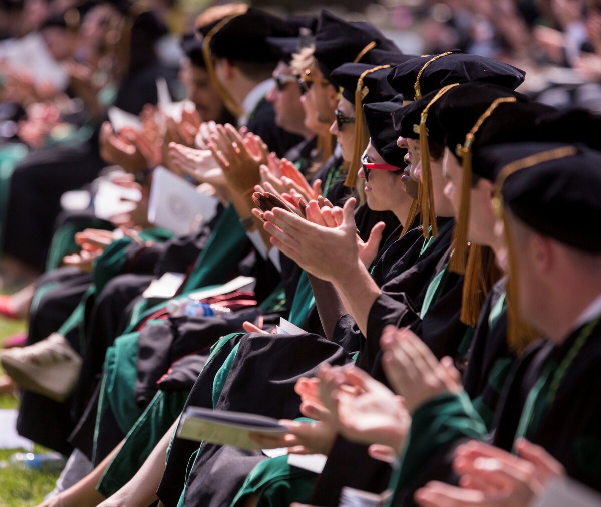 A group of CMSRU graduates clapping while sitting in regalia at a CMSRU Commencement ceremony.