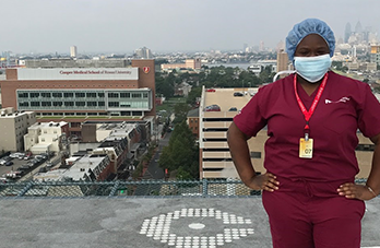 A student is shown standing in scrubs.