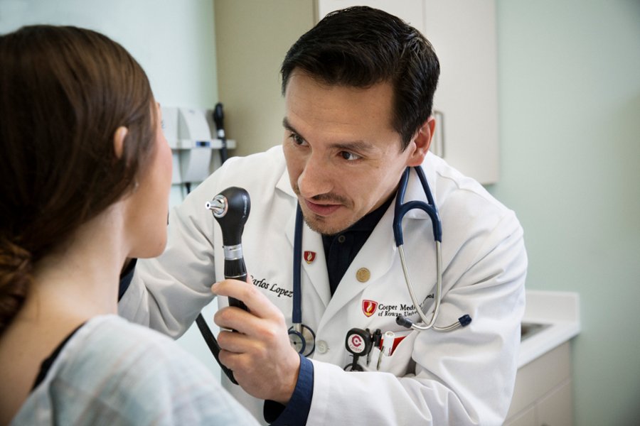 A male student uses an otoscope to look in the nose of a female standardized patient.