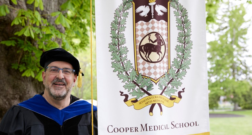 Russell Buono, PhD, professor of biomedical sciences at CMSRU poses with the CMSRU gonfalon at the CMSRU Commencement ceremony.