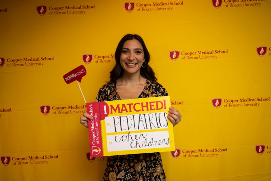 A CMSRU student poses with a sign featuring their Match during CMSRU's Match Day celebration.