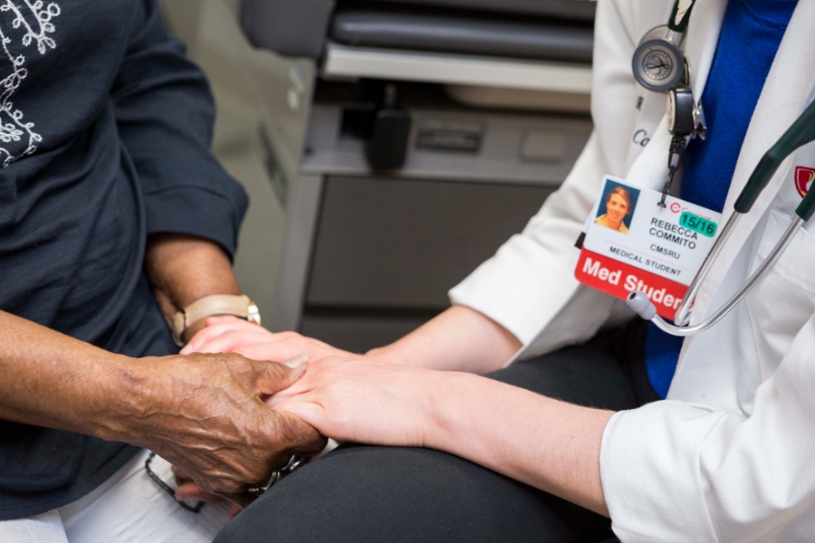 A CMSRU student empathetically holds a patient's hand.